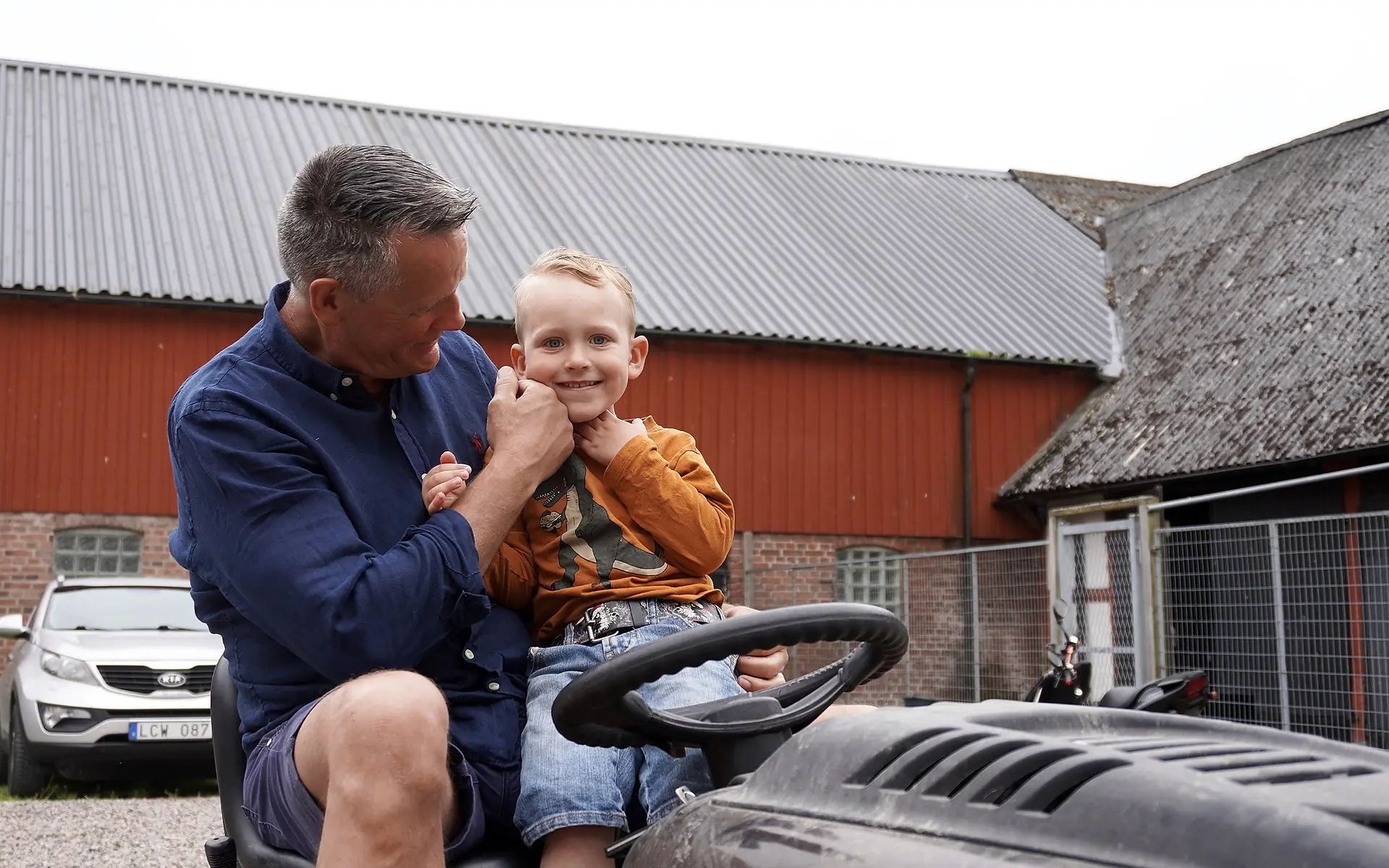 Mats Svensson med ett barn utomhus framför en röd ekonomibyggnad.
